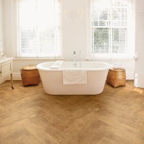 Wood effect flooring laid in a herringbone style bathroom with a white bath