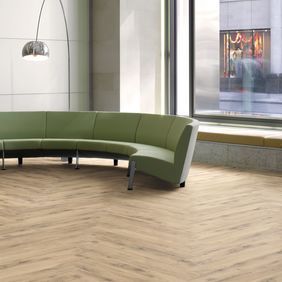 Light brown oak effect flooring in a herringbone design with a green curved sofa 