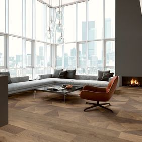 Mixed style oak effect flooring in an apartment with floor to ceiling windows and a large grey couch