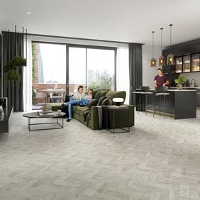 Oak effect parquet flooring laid in an open living/ dining area with people sat on the couch