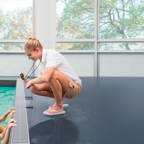 Dark blue safety flooring around a public swimming pool with children and instructor