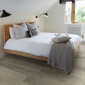 Light oak effect flooring in a residential bedroom with a wooden bed and white bedding