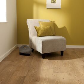 Oak effect flooring laid in a room with yellow walls and a cream arm chair