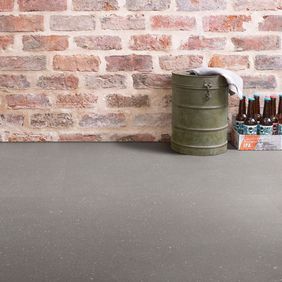 Grey coloured flooring laid in a room with open red brick walls as some beer bottles on the floor