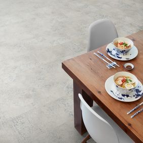 Close up of the corner of a dining table with chairs featuring light concrete effect flooring