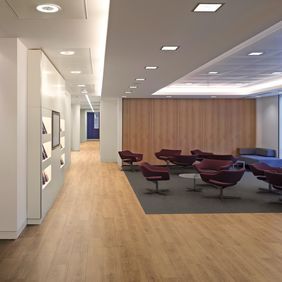 light oak effect flooring and Rich oak effect flooring used to create zonal space waiting area with small table and lounge chairs
