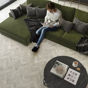 Oak effect parquet flooring lain in a living space with a person sat on a green couch