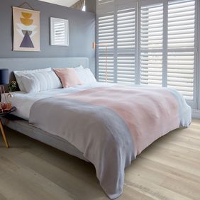 Light wood effect flooring with a kingsize bed with grey and pink accessories 
