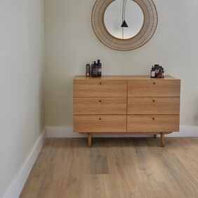 Oak effect flooring laid straight in a room with a mirror on the wall and a wooden set of drawers