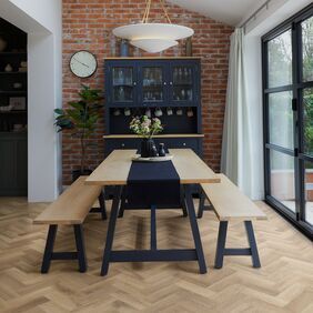 Light coloured oak effect flooring laid in a small parquet style in a modern kitchen/ diner with a oak and black bench