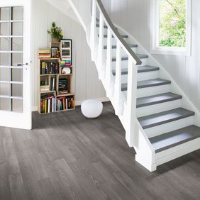 Dark oak wood effect flooring in a hallway with a bookshelf and quirky staircase