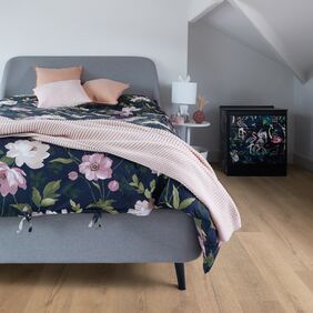 Oak effect flooring laid in a bedroom with a grey fabric bed and floral bedding