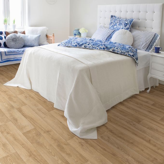 Light oak wood effect flooring in a bedroom with a large white bed and light blue accessories 