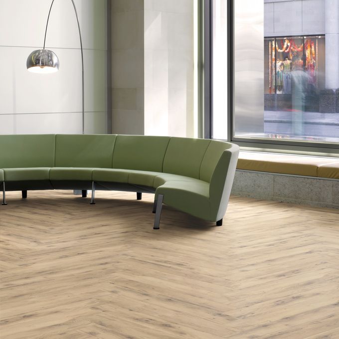 Light brown oak effect flooring in a herringbone design with a green curved sofa 