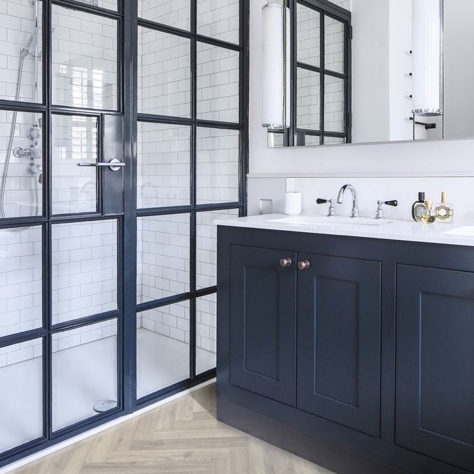 Oak effect flooring laid in a herringbone style in a bathroom with dark coloured units and a walk in shower