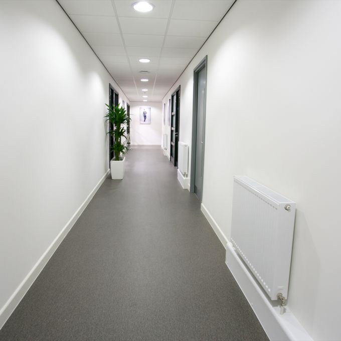 Grey stone effect safety flooring in a corridor with white walls and floor plants 