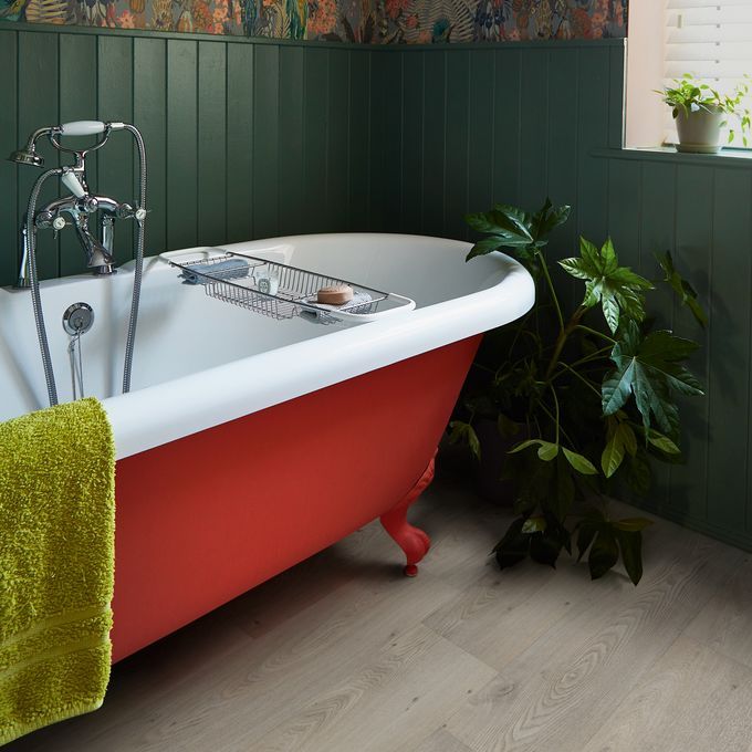 Oak effect flooring in a bathroom with a red panel bath