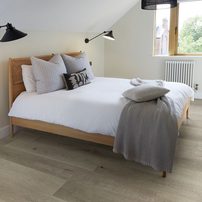 Light oak effect flooring in a residential bedroom with a wooden bed and white bedding