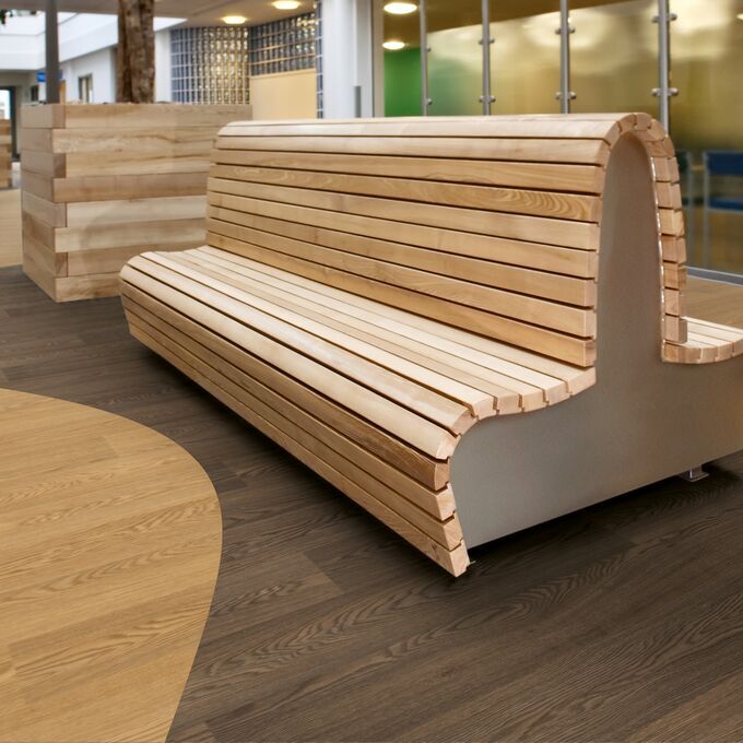 Light and dark coloured wood effect flooring in a building corridor with a wooden bench