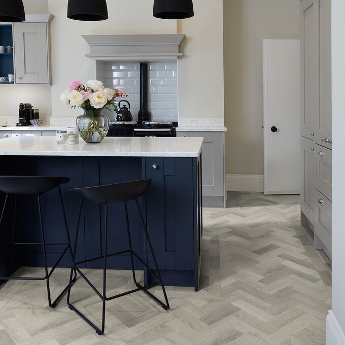 Light coloured oak effect flooringlaid in a small parquet style in a kitchen with blue cupboards and white worktops