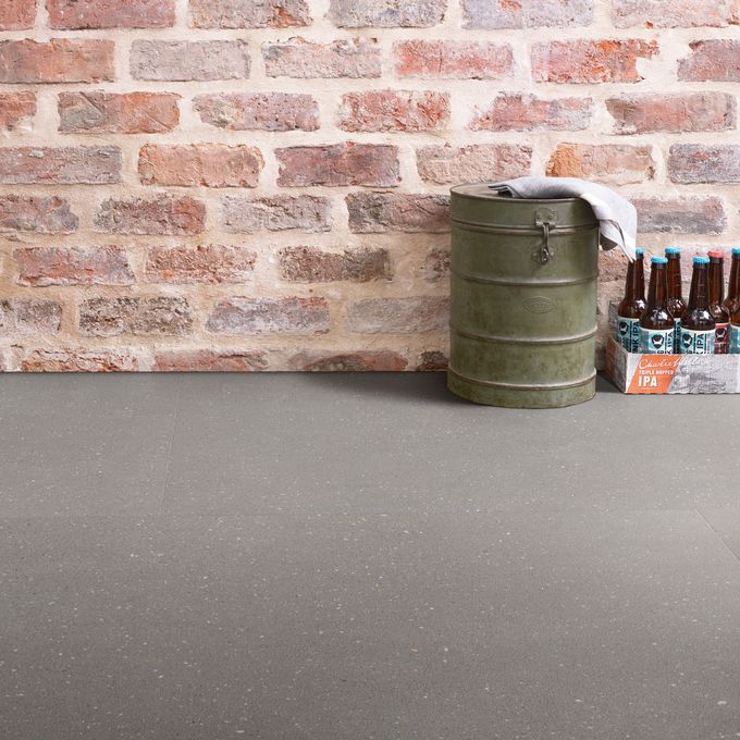 Grey coloured flooring laid in a room with open red brick walls as some beer bottles on the floor