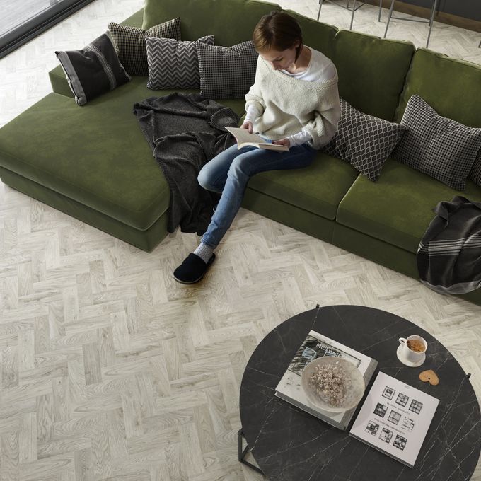 Oak effect parquet flooring lain in a living space with a person sat on a green couch