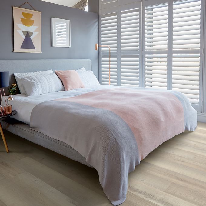 Light wood effect flooring with a kingsize bed with grey and pink accessories 