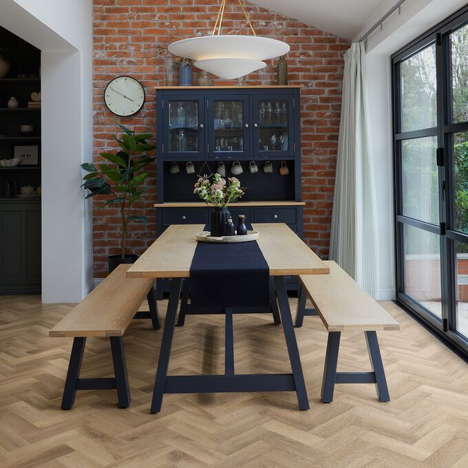Light coloured oak effect flooring laid in a small parquet style in a modern kitchen/ diner with a oak and black bench