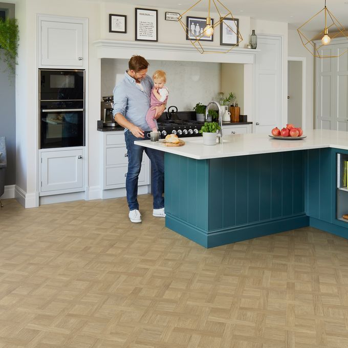Wood effect flooring in a basket weave style laid in a large kitchen where a man is stood holding a toddler