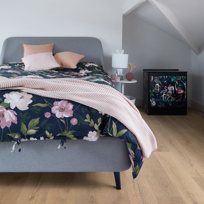 Oak effect flooring laid in a bedroom with a grey fabric bed and floral bedding